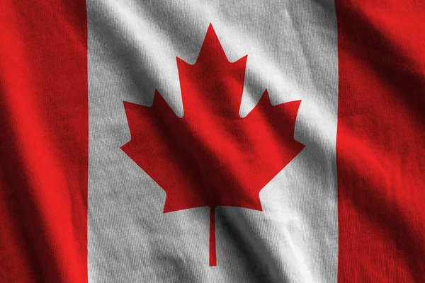 Canada flag with big folds waving close up under the studio light indoors. The official symbols and colors in fabric banner