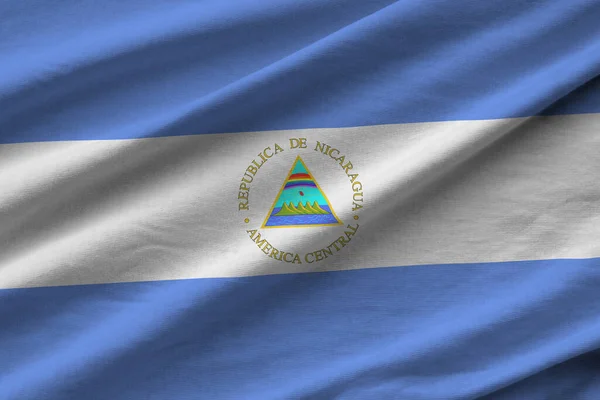 スタジオの光の下で屋内で手を振る大きな折り目のあるニカラグアの旗 ファブリックバナーの公式シンボルと色 — ストック写真