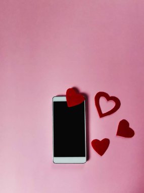 Pembe bir arka planda, keçeden yapılmış kırmızı kalpler ve boş bir akıllı telefon ekranı, boş fotokopi alanı, yaratıcı bir model fikri