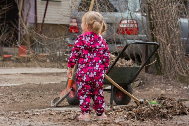 İki yaşındaki bir kız yaprakları süpürgeyle tek başına topluyor.
