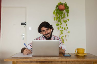 Evde dizüstü bilgisayar ve kağıtlarla çalışan genç bir iş adamı. Çalışanlar için gri defter ve beyaz kulaklıklar. Merkez ofis konsepti. Yüksek kalite fotoğraf