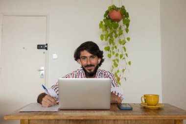 Evde dizüstü bilgisayar ve kağıtlarla çalışan genç bir iş adamı. Çalışanlar için gri defter ve beyaz kulaklıklar. Merkez ofis konsepti. Yüksek kalite fotoğraf