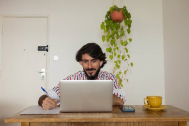 Evde dizüstü bilgisayar ve kağıtlarla çalışan genç bir iş adamı. Çalışanlar için gri defter ve beyaz kulaklıklar. Merkez ofis konsepti. Yüksek kalite fotoğraf