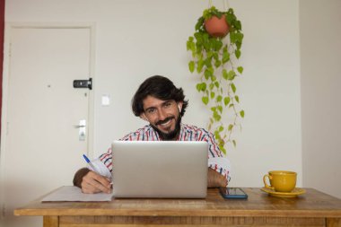 Evde dizüstü bilgisayar ve kağıtlarla çalışan genç bir iş adamı. Çalışanlar için gri defter ve beyaz kulaklıklar. Merkez ofis konsepti. Yüksek kalite fotoğraf