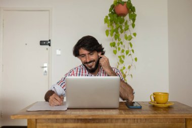 Evde dizüstü bilgisayar ve kağıtlarla çalışan genç bir iş adamı. Çalışanlar için gri defter ve beyaz kulaklıklar. Merkez ofis konsepti. Yüksek kalite fotoğraf