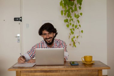 Genç bir iş adamı evinde dizüstü bilgisayarla kahverengi bir koltukta çalışıyor. Çalışmak için gri defter. Merkez ofis konsepti. Yüksek kalite fotoğraf