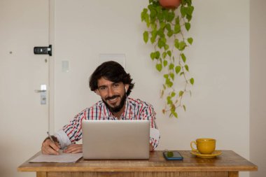 Genç bir iş adamı evinde dizüstü bilgisayarla kahverengi bir koltukta çalışıyor. Çalışmak için gri defter. Merkez ofis konsepti. Yüksek kalite fotoğraf