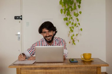 Genç bir iş adamı evinde dizüstü bilgisayarla kahverengi bir koltukta çalışıyor. Çalışmak için gri defter. Merkez ofis konsepti. Yüksek kalite fotoğraf