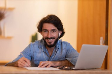 Evde dizüstü bilgisayar ve kağıtlarla çalışan genç bir iş adamı. Çalışanlar için gri defter ve beyaz kulaklıklar. Merkez ofis konsepti. Yüksek kalite fotoğraf