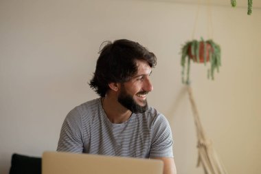 Genç bir iş adamı mutfakta dizüstü bilgisayarla ve mutfak masasında kağıtlarla çalışıyor. Çalışmak için gri defter. Merkez ofis konsepti. Yüksek kalite fotoğraf