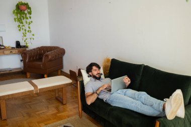 Oturma odasındaki kanepede dizüstü bilgisayarla çalışan genç bir iş adamı. Yerde yatan adam. Çalışmak için gri defter. Yeşil koltuk. Merkez ofis konsepti. Yüksek kalite fotoğraf