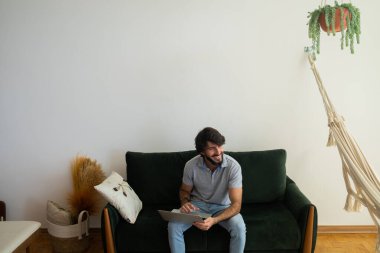 Oturma odasındaki kanepede dizüstü bilgisayarla çalışan genç bir iş adamı. Çalışmak için gri defter. Merkez ofis konsepti. Yüksek kalite fotoğraf