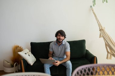 Oturma odasındaki kanepede dizüstü bilgisayarla çalışan genç bir iş adamı. Çalışmak için gri defter. Merkez ofis konsepti. Yüksek kalite fotoğraf