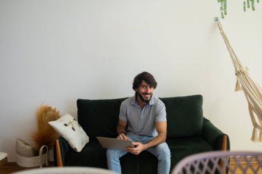 Oturma odasındaki kanepede dizüstü bilgisayarla çalışan genç bir iş adamı. Çalışmak için gri defter. Merkez ofis konsepti. Yüksek kalite fotoğraf