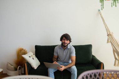 Oturma odasındaki kanepede dizüstü bilgisayarla çalışan genç bir iş adamı. Çalışmak için gri defter. Merkez ofis konsepti. Yüksek kalite fotoğraf