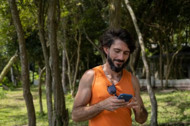Güzel güneşli bir günde, cep telefonuyla parkta genç bir adam. Çalışmak ve rahatlamak için cep telefonu. Merkez ofis konsepti. Yeşil ve doğa geçmişi. Yüksek kalite fotoğraf