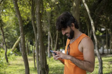 Güzel güneşli bir günde, cep telefonuyla parkta genç bir adam. Çalışmak ve rahatlamak için cep telefonu. Merkez ofis konsepti. Yeşil ve doğa geçmişi. Yüksek kalite fotoğraf