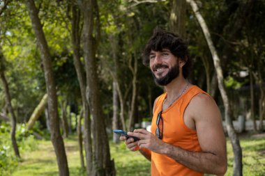Güzel güneşli bir günde, cep telefonuyla parkta genç bir adam. Çalışmak ve rahatlamak için cep telefonu. Merkez ofis konsepti. Yeşil ve doğa geçmişi. Yüksek kalite fotoğraf