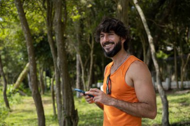 Güzel güneşli bir günde, cep telefonuyla parkta genç bir adam. Çalışmak ve rahatlamak için cep telefonu. Merkez ofis konsepti. Yeşil ve doğa geçmişi. Yüksek kalite fotoğraf