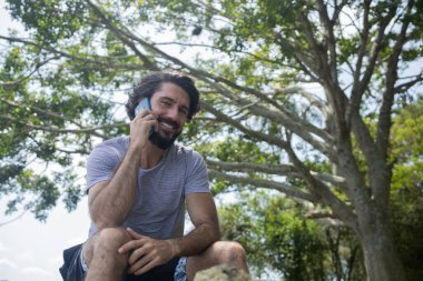 Güzel güneşli bir günde, cep telefonuyla parkta genç bir adam. Çalışmak ve rahatlamak için cep telefonu. Merkez ofis konsepti. Yeşil ve doğa geçmişi. Yüksek kalite fotoğraf