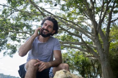 Güzel güneşli bir günde, cep telefonuyla parkta genç bir adam. Çalışmak ve rahatlamak için cep telefonu. Merkez ofis konsepti. Yeşil ve doğa geçmişi. Yüksek kalite fotoğraf
