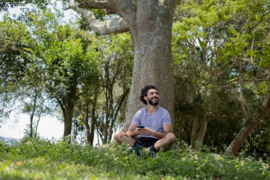 Güzel güneşli bir günde, cep telefonuyla parkta genç bir adam. Çalışmak ve rahatlamak için cep telefonu. Merkez ofis konsepti. Yeşil ve doğa geçmişi. Yüksek kalite fotoğraf