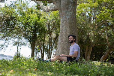 Güzel, güneşli bir günde kucağında dizüstü bilgisayarla parkta genç bir adam. Çalışmak ve boş vakit geçirmek için gri defter. Merkez ofis konsepti. Yeşil ve doğa geçmişi. Yüksek kalite fotoğraf