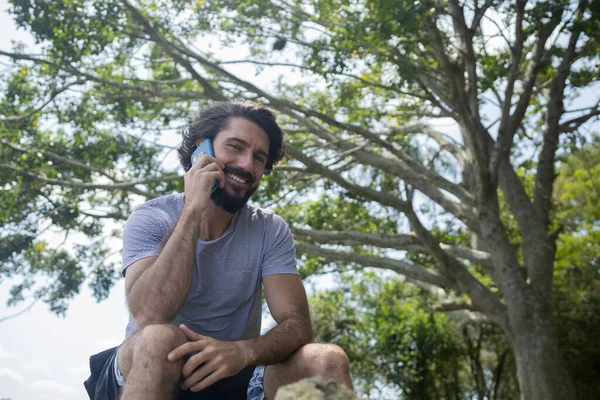 Güzel güneşli bir günde, cep telefonuyla parkta genç bir adam. Çalışmak ve rahatlamak için cep telefonu. Merkez ofis konsepti. Yeşil ve doğa geçmişi. Yüksek kalite fotoğraf