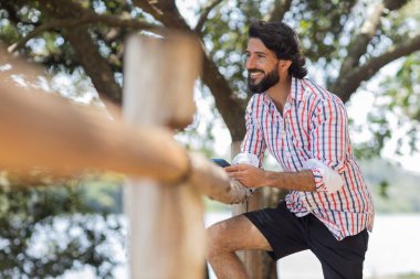 Güzel güneşli bir günde, cep telefonuyla parkta genç bir adam. Çalışmak ve rahatlamak için cep telefonu. Merkez ofis konsepti. Yeşil ve doğa geçmişi. Yüksek kalite fotoğraf
