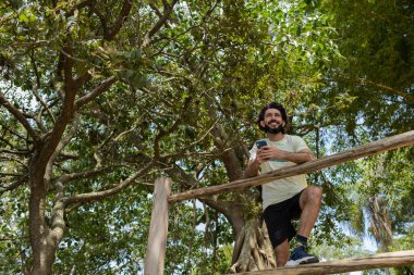 Güzel güneşli bir günde, cep telefonuyla parkta genç bir adam. Çalışmak ve rahatlamak için cep telefonu. Merkez ofis konsepti. Yeşil ve doğa geçmişi. Yüksek kalite fotoğraf