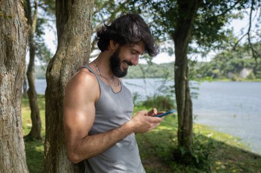 Güzel güneşli bir günde, cep telefonuyla parkta genç bir adam. Çalışmak ve rahatlamak için cep telefonu. Merkez ofis konsepti. Yeşil ve doğa geçmişi. Yüksek kalite fotoğraf