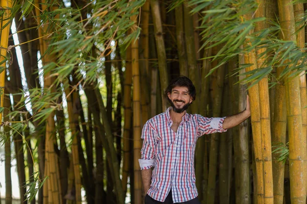 Güneşli bir günde parktaki gülümseyen genç adamın portresi. Yeşil ve doğa geçmişi. Bambu ormanı. Yüksek kalite fotoğraf