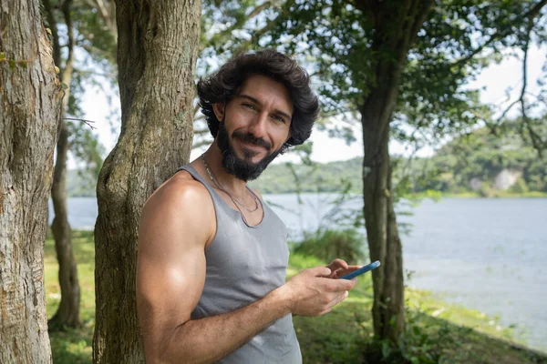 stock image Young man at a park on a beautiful sunny day with mobile phone. Mobile phone for working and leisure. Home office concept. Green and nature background. High quality photo