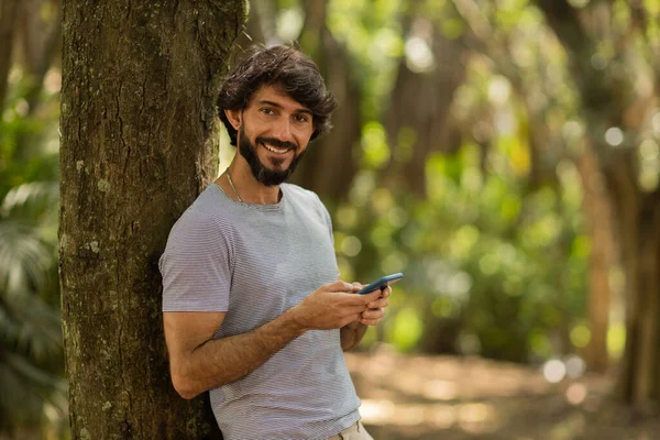 Gündüz vakti arka planda yeşil park olan akıllı telefon kullanan genç bir adamın görüntüsü. Cep telefonu, teknoloji, şehir konsepti. Yüksek kalite fotoğraf