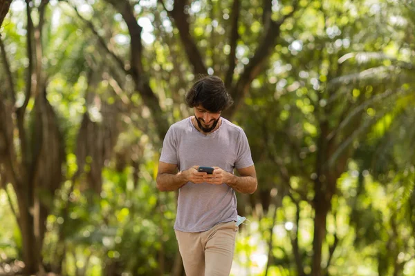 Gündüz vakti arka planda yeşil park olan akıllı telefon kullanan genç bir adamın görüntüsü. Cep telefonu, teknoloji, şehir konsepti. Yüksek kalite fotoğraf