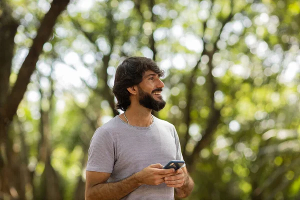 Gündüz vakti arka planda yeşil park olan akıllı telefon kullanan genç bir adamın görüntüsü. Cep telefonu, teknoloji, şehir konsepti. Yüksek kalite fotoğraf