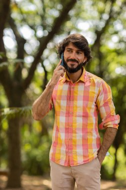Gündüz vakti arka planda yeşil park olan akıllı telefon kullanan genç bir adamın görüntüsü. Cep telefonu, teknoloji, şehir konsepti. Yüksek kalite fotoğraf