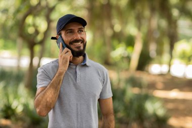 Gündüz vakti arka planda yeşil park olan akıllı telefon kullanan genç bir adamın görüntüsü. Cep telefonu, teknoloji, şehir konsepti. Yüksek kalite fotoğraf
