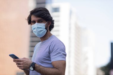 Gündüz vakti akıllı telefon kullanan ve arka planda şehir manzaralı genç bir adamın görüntüsü. Cep telefonu, teknoloji, şehir konsepti. Yüksek kalite fotoğraf