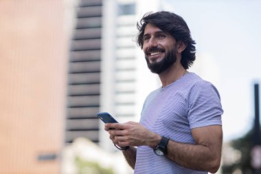Gündüz vakti akıllı telefon kullanan ve arka planda şehir manzaralı genç bir adamın görüntüsü. Cep telefonu, teknoloji, şehir konsepti. Yüksek kalite fotoğraf
