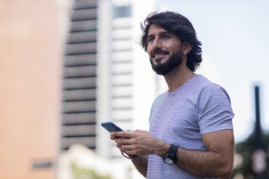 Gündüz vakti akıllı telefon kullanan ve arka planda şehir manzaralı genç bir adamın görüntüsü. Cep telefonu, teknoloji, şehir konsepti. Yüksek kalite fotoğraf
