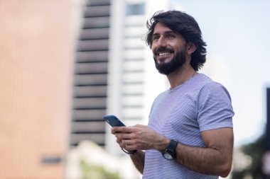 Gündüz vakti akıllı telefon kullanan ve arka planda şehir manzaralı genç bir adamın görüntüsü. Cep telefonu, teknoloji, şehir konsepti. Yüksek kalite fotoğraf