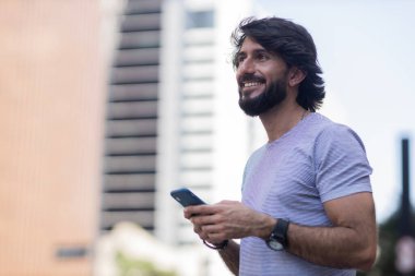 Gündüz vakti akıllı telefon kullanan ve arka planda şehir manzaralı genç bir adamın görüntüsü. Cep telefonu, teknoloji, şehir konsepti. Yüksek kalite fotoğraf