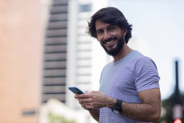 Gündüz vakti akıllı telefon kullanan ve arka planda şehir manzaralı genç bir adamın görüntüsü. Cep telefonu, teknoloji, şehir konsepti. Yüksek kalite fotoğraf