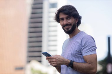 Gündüz vakti akıllı telefon kullanan ve arka planda şehir manzaralı genç bir adamın görüntüsü. Cep telefonu, teknoloji, şehir konsepti. Yüksek kalite fotoğraf