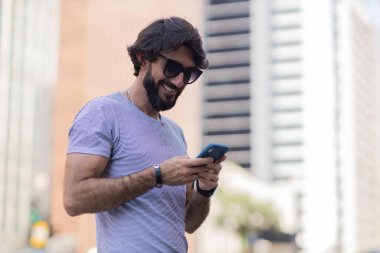Gündüz vakti akıllı telefon kullanan ve arka planda şehir manzaralı genç bir adamın görüntüsü. Cep telefonu, teknoloji, şehir konsepti. Yüksek kalite fotoğraf