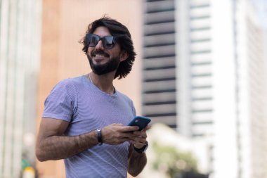 Gündüz vakti akıllı telefon kullanan ve arka planda şehir manzaralı genç bir adamın görüntüsü. Cep telefonu, teknoloji, şehir konsepti. Yüksek kalite fotoğraf