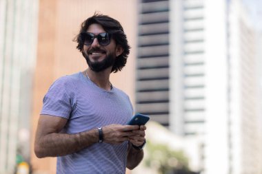Gündüz vakti akıllı telefon kullanan ve arka planda şehir manzaralı genç bir adamın görüntüsü. Cep telefonu, teknoloji, şehir konsepti. Yüksek kalite fotoğraf
