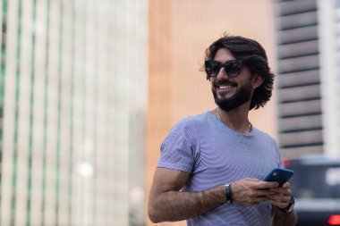 Gündüz vakti akıllı telefon kullanan ve arka planda şehir manzaralı genç bir adamın görüntüsü. Cep telefonu, teknoloji, şehir konsepti. Yüksek kalite fotoğraf