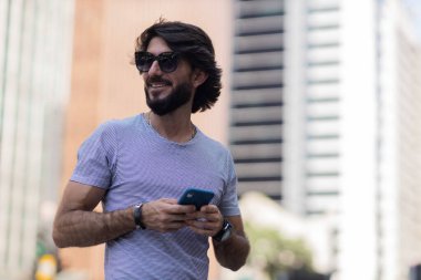 Gündüz vakti akıllı telefon kullanan ve arka planda şehir manzaralı genç bir adamın görüntüsü. Cep telefonu, teknoloji, şehir konsepti. Yüksek kalite fotoğraf